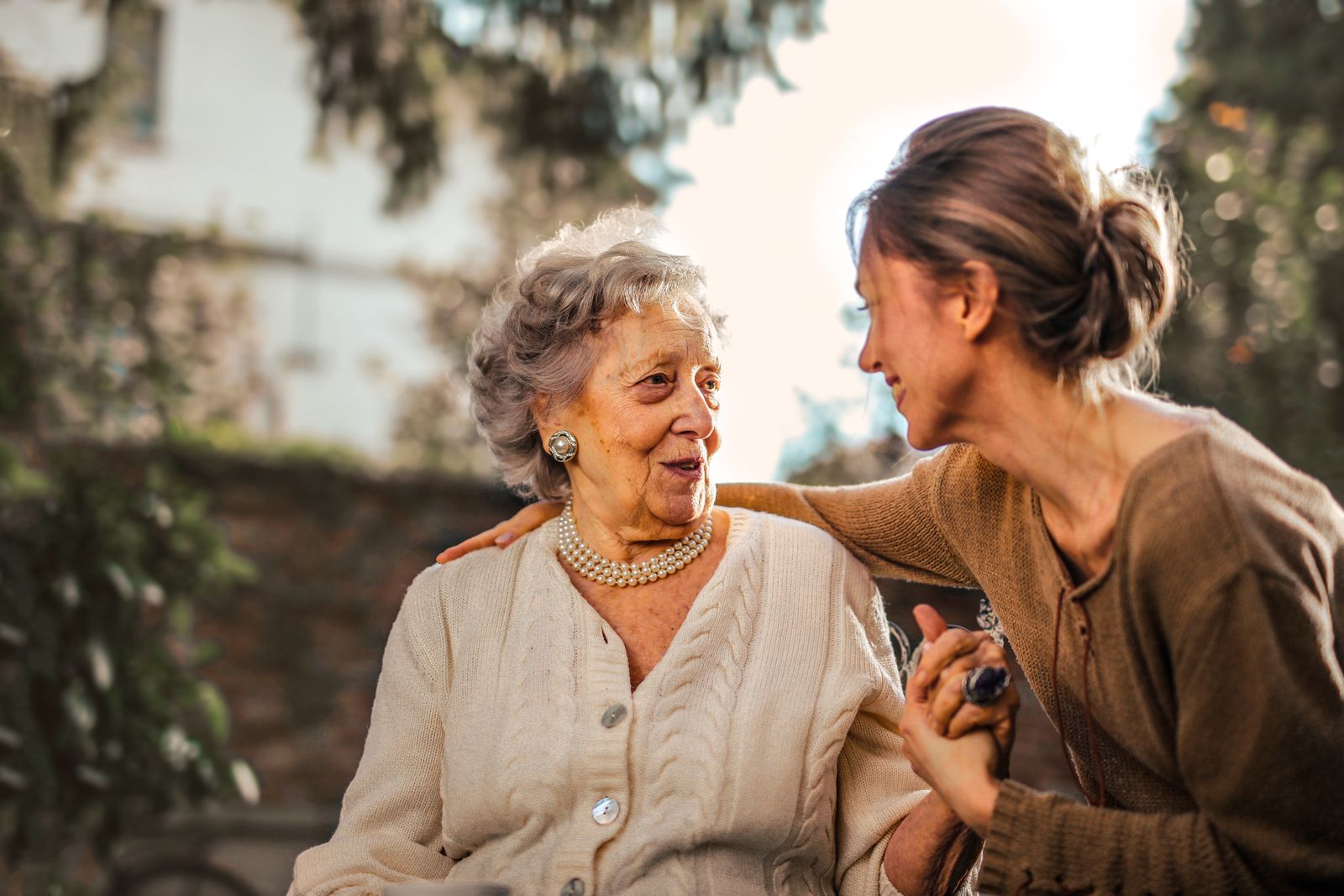 A caregiver embracing a smiling older woman in a sunlit garden